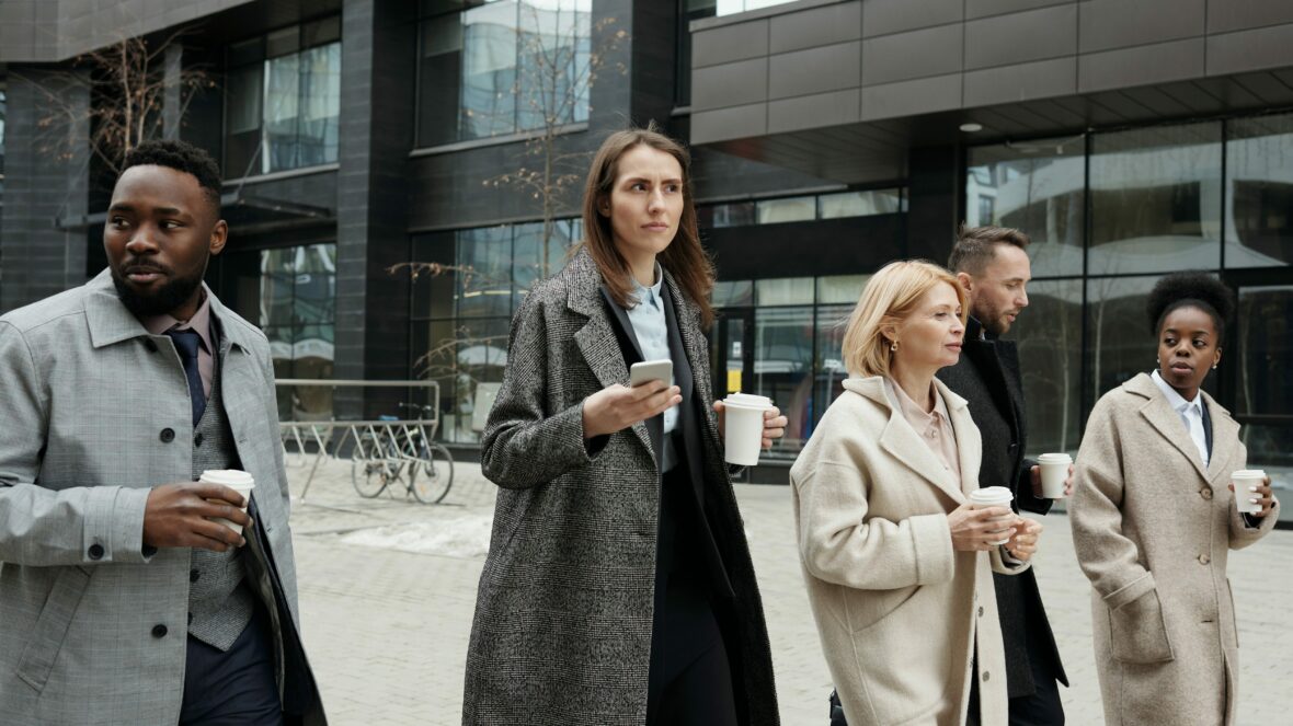 Tre kvinnor och två män med kaffemuggar går genom stadsmiljö