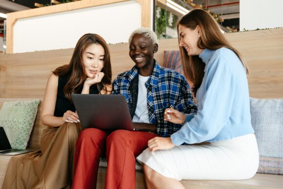 Tre glada kvinnor samlade runt laptop