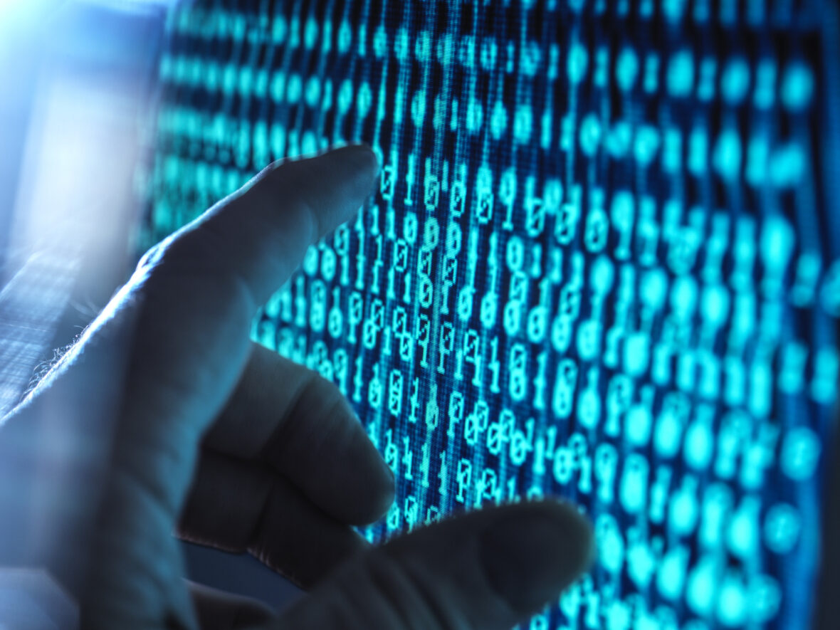 BIld på dataskärm med ettor och nollor en hand pekar på skärmen. bilden försöker förmedla en känsla av analys.